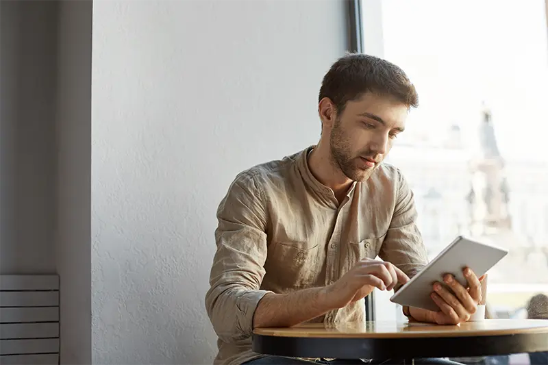 hubscher bartiger mann mit kurzen haaren der freizeitkleidung die im cafe sitzt und details des startprojekts auf tablette durchschaut unternehmenskonzept 1